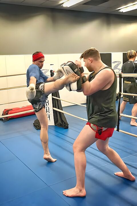 A Rumble striking coach throwing a teep kick on the pads in the ring at Keswick.