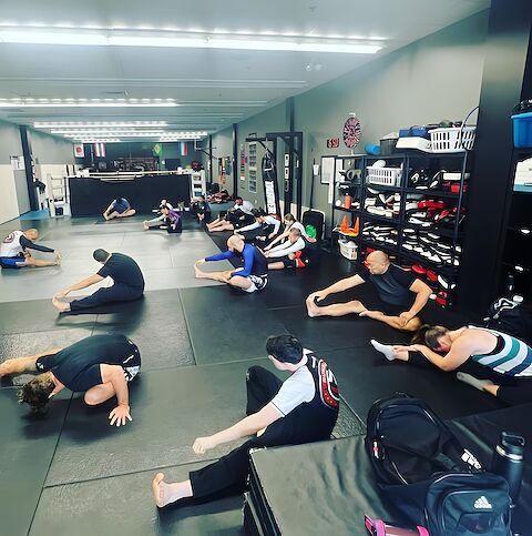 The adult grappling class stretching through the warm-up.