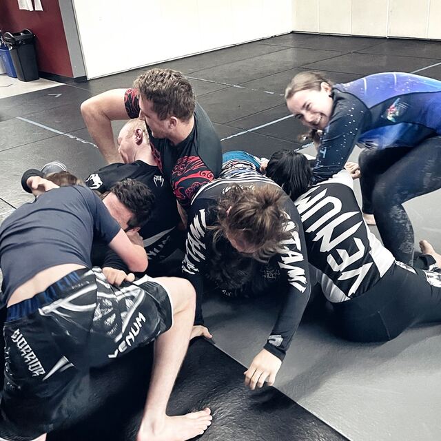 A group of adult Brazilian jiu-jitsu students grappling together on the mats at Rumble Martial Arts.
