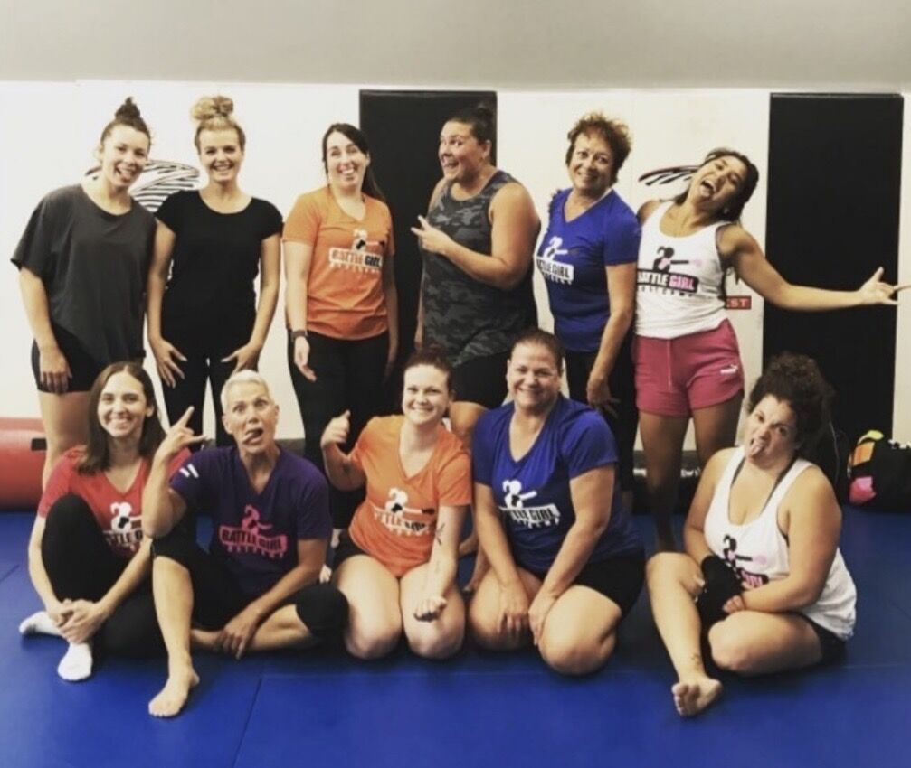 A Battle Girl Bootcamp class posing together in their Battle Girl shirts on the blue mats at Rumble Martial Arts.