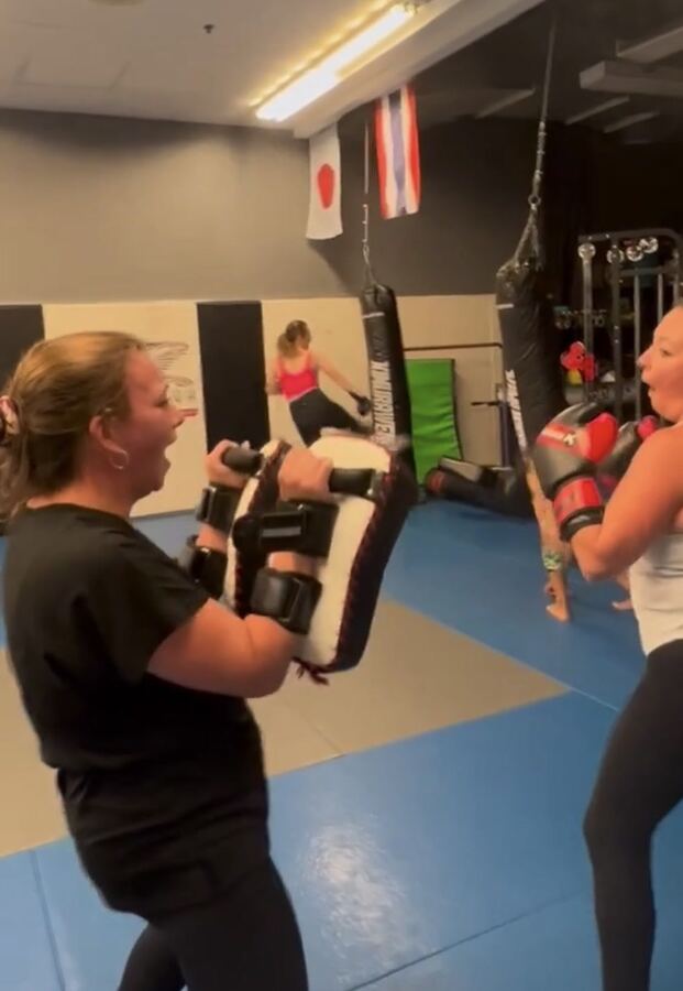 A woman holding Thai pads for another woman's cross punch in a women-only bootcamp class