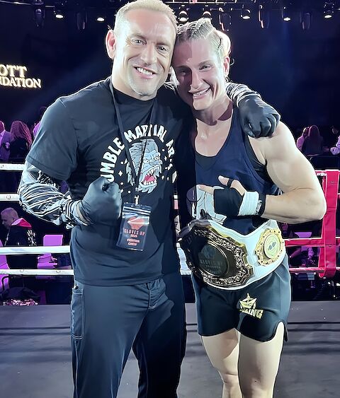 Kru Jones in the ring with one of his fighters holding her championship belt.