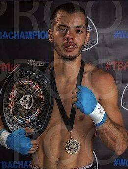 Coach Spyros after a fight, shirtless in blue hand wraps, holding a championship belt with a medal around his neck.