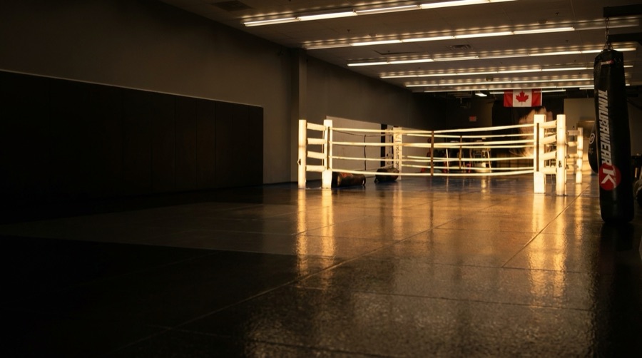 The empty gym at golden hour, showing the black mats and white boxing ring where birthday parties are held.