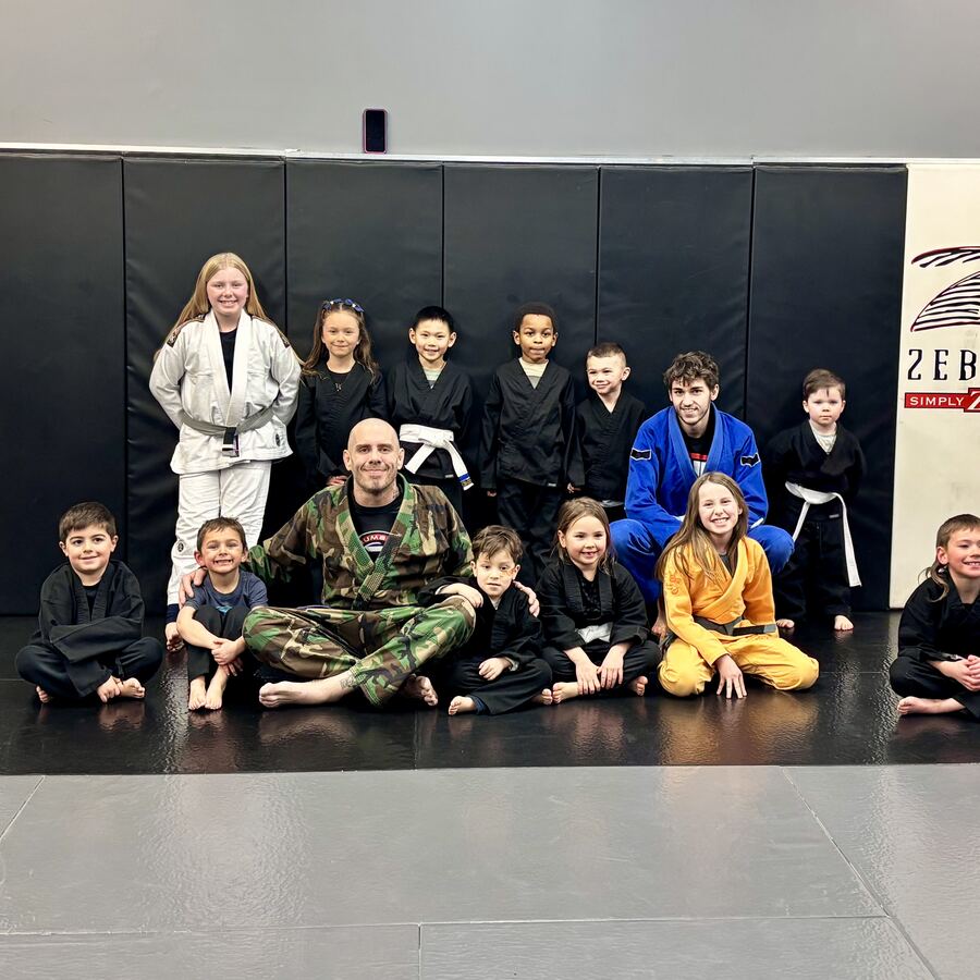 A kids jiu-jitsu class group photo in gis with their coach on the mats at Rumble Martial Arts in Keswick.