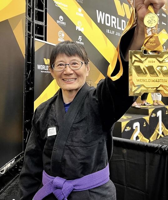 Coach Gladys holding up her IBJJF World Master gold medal on the podium.