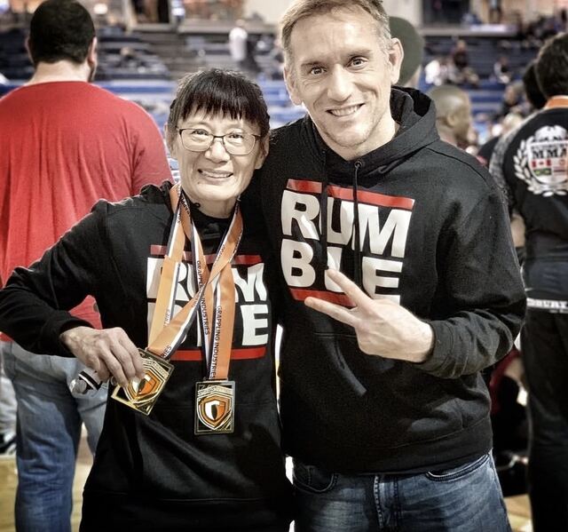 Coach Gladys with her medals, next to Professor Jones in a Rumble hoodie.